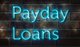Image of the words "Payday Loans" in blue neon against a brick wall [Image by creator Rex Wholster from AdobeStock]